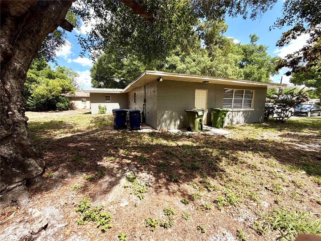 A single-story brick house with a flat roof, two trash bins, and a large tree — 1405 AVENUE H SW, WINTER HAVEN, FL