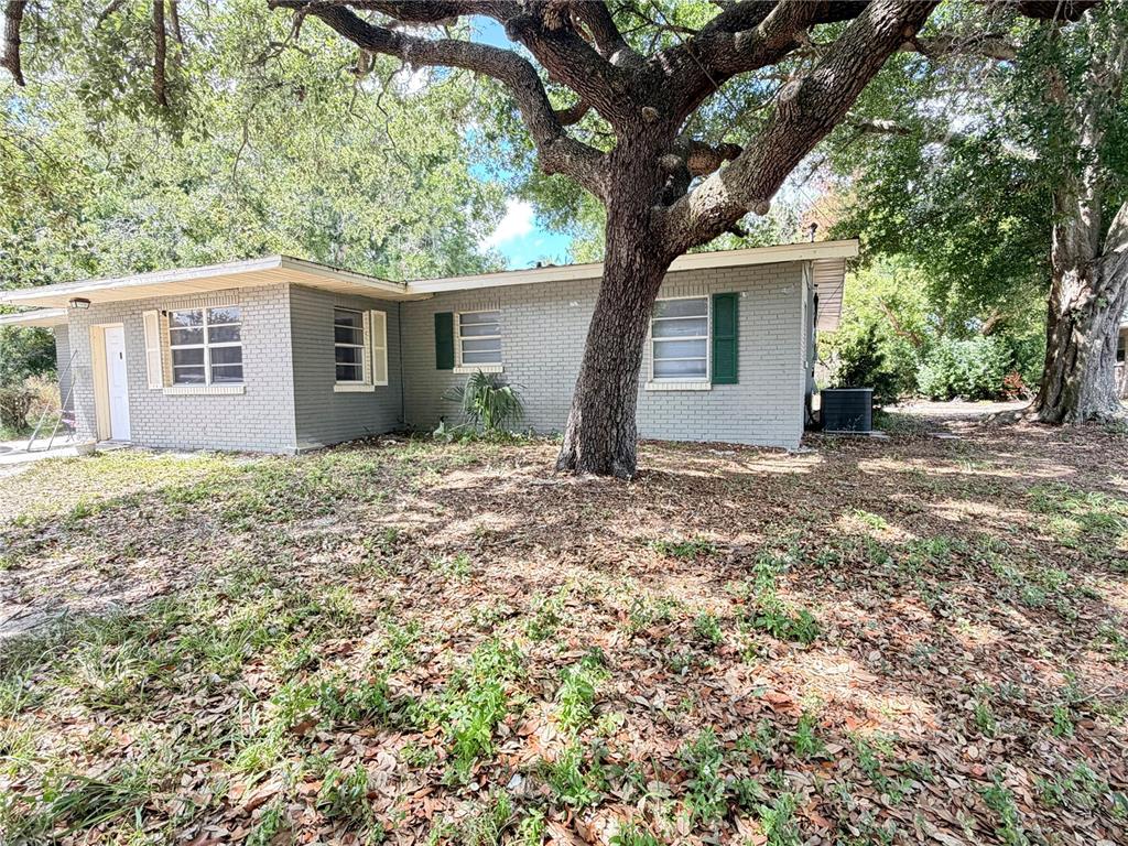 A single-story gray brick house with green shutters sits under a large oak tree — 1405 AVENUE H SW, WINTER HAVEN, FL