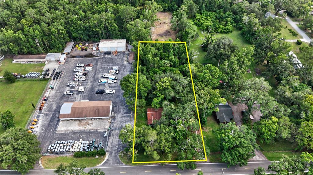 An aerial view shows a rectangular, tree-covered lot outlined in yellow next to a parking lot — 19370 FORT DADE AVENUE, BROOKSVILLE, FL