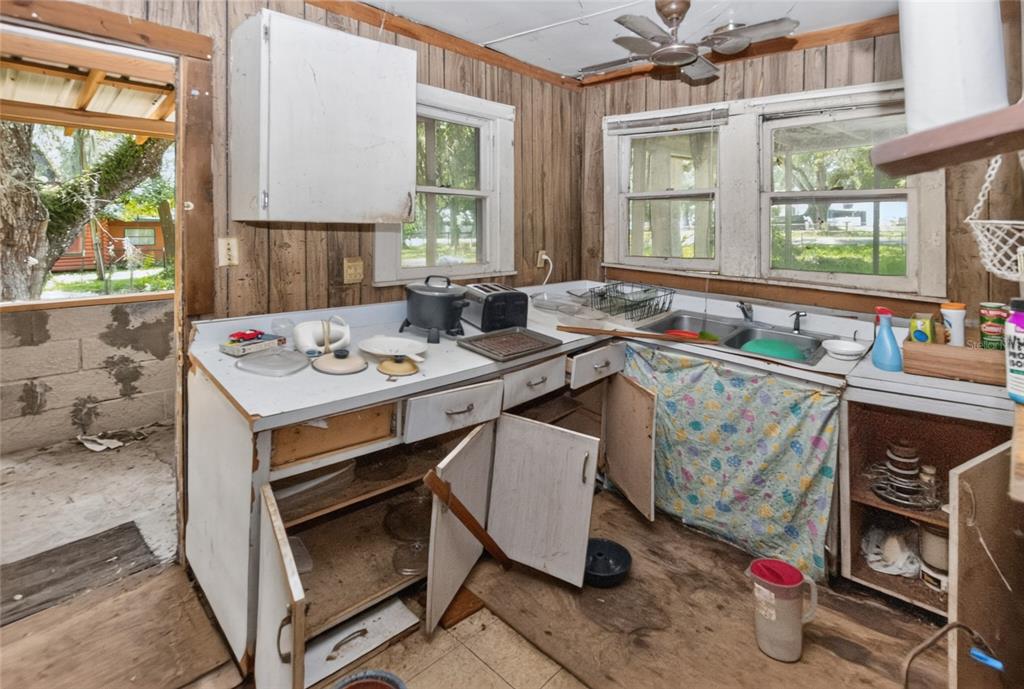 A rustic kitchen with wood-paneled walls, worn cabinetry, and an open doorway to the outdoors — 19370 FORT DADE AVENUE, BROOKSVILLE, FL