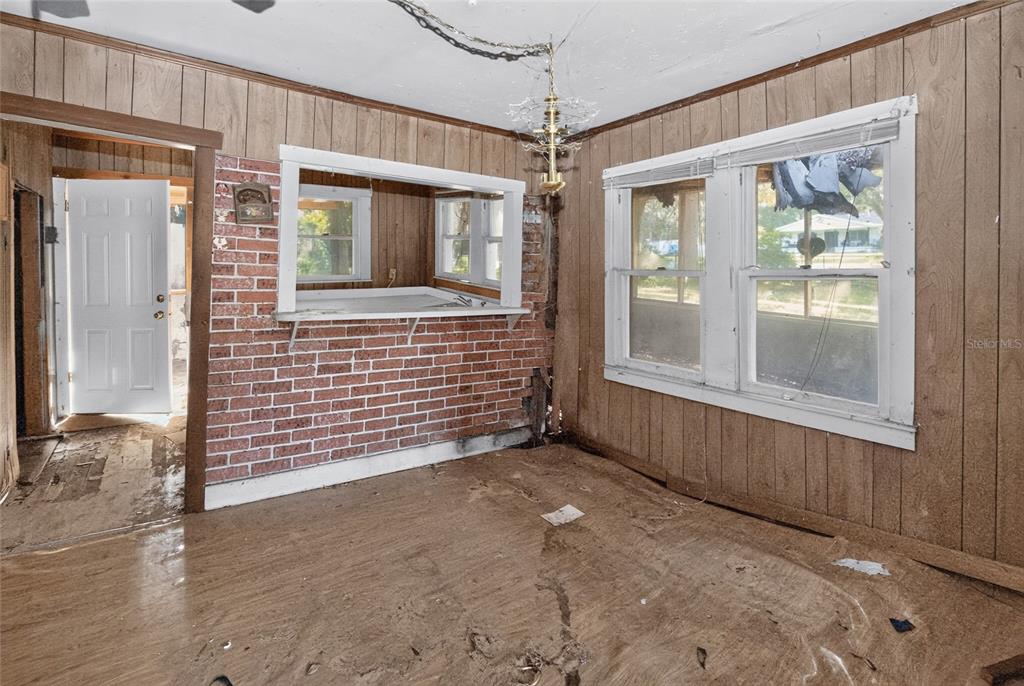 A room with wood-paneled walls, a brick pass-through window, and damaged flooring — 19370 FORT DADE AVENUE, BROOKSVILLE, FL