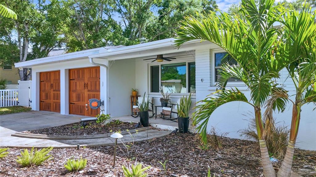 A white house exterior features two wooden garage doors, a covered porch, and palm trees — 101 N MERCURY AVENUE, CLEARWATER, FL