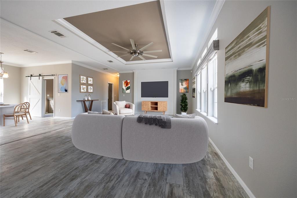 A living room with a tray ceiling, light wood-look flooring, and a large gray sofa — 6671 SW 128TH LANE, LAKE BUTLER, FL