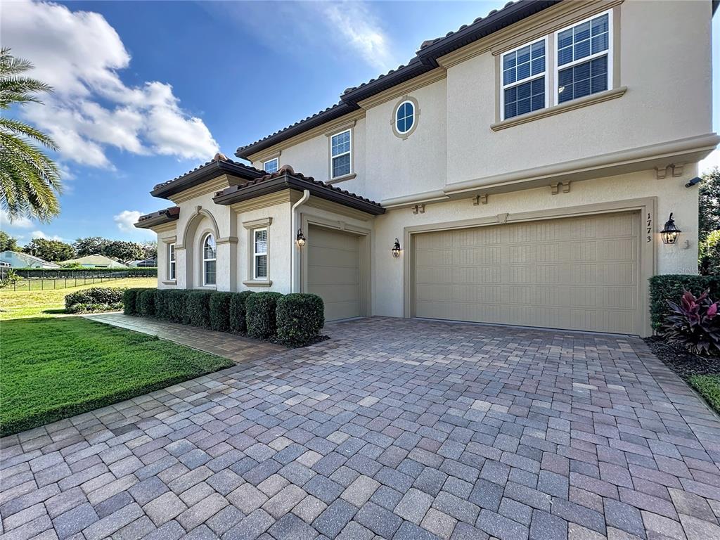 A two-story suburban house with a tan stucco exterior, tile roof, and brick paver driveway — 1773 BELLA LAGO DRIVE, CLERMONT, FL