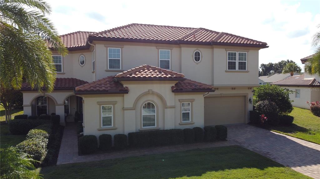 A two-story house with a beige stucco exterior, a tiled roof, and a paved driveway — 1773 BELLA LAGO DRIVE, CLERMONT, FL