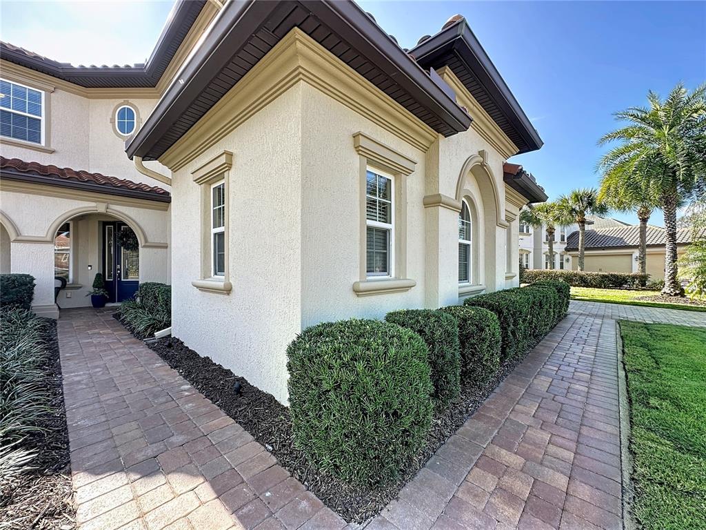 A stucco house exterior features a brick walkway, manicured hedges, and dark roof eaves — 1773 BELLA LAGO DRIVE, CLERMONT, FL