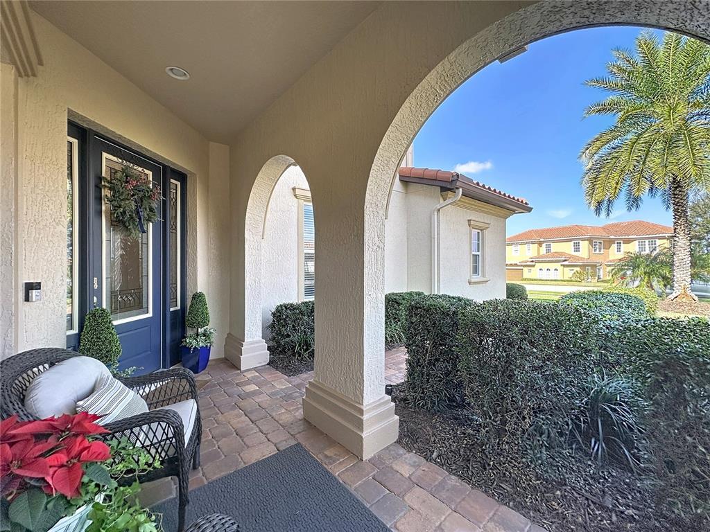 A covered front porch features arched columns, brick pavers, and a dark blue front door — 1773 BELLA LAGO DRIVE, CLERMONT, FL