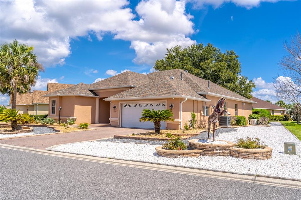 A tan single-story house features a two-car garage, a horse statue, and white gravel landscaping — 8508 SW 84TH LOOP, OCALA, FL