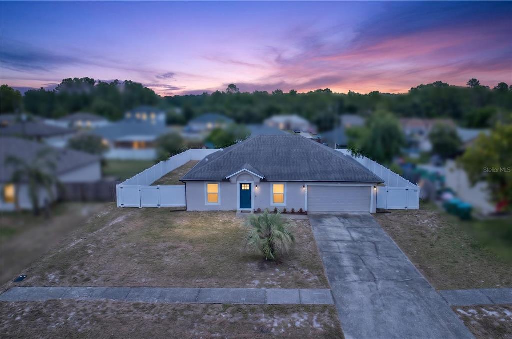 A single-story house with a gray roof, white fence, and a concrete driveway at dusk — 2918 CHALMER STREET, DELTONA, FL
