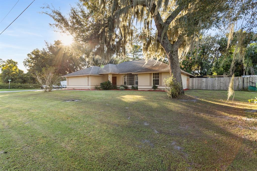 A single-story house with a tan exterior and a large oak tree in the yard — 1191 S BRICKELL DRIVE, DELTONA, FL