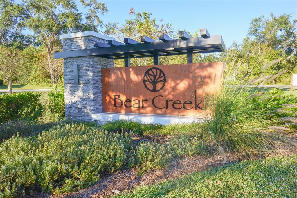 A stone and metal monument sign for Bear Creek stands in a landscaped garden area — 12016 GRIZZLY LANE, NEW PORT RICHEY, FL