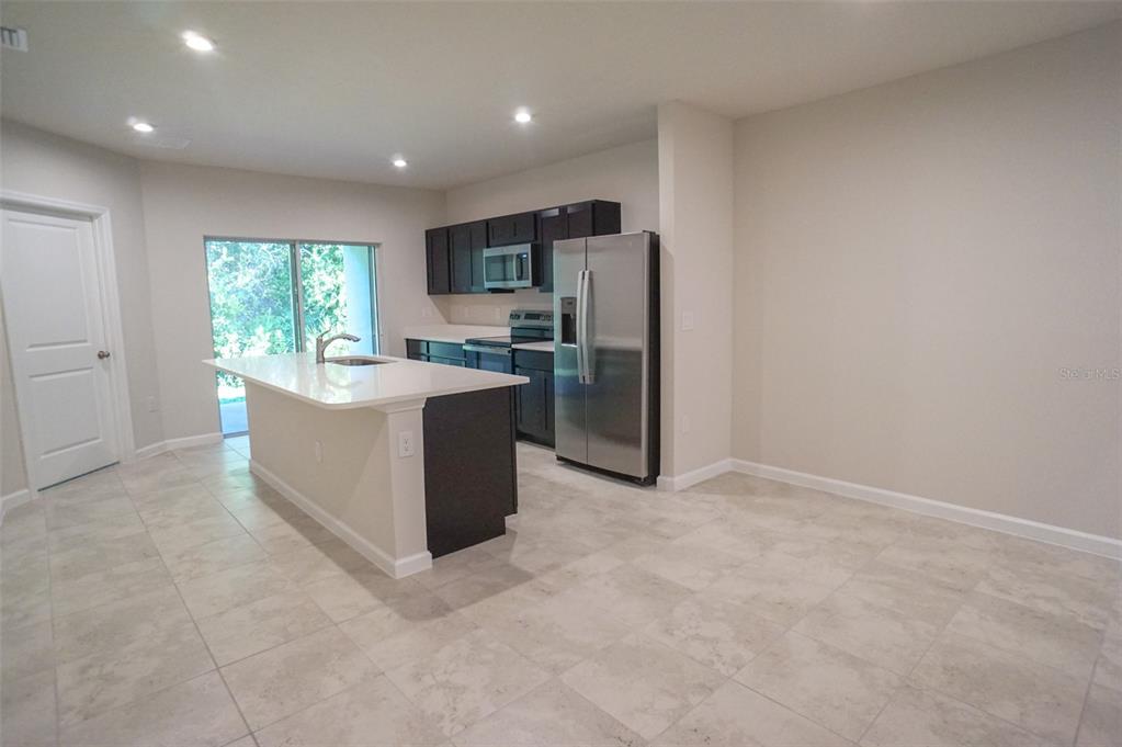 A kitchen features dark cabinetry, stainless steel appliances, a white island, and light tile flooring — 12016 GRIZZLY LANE, NEW PORT RICHEY, FL