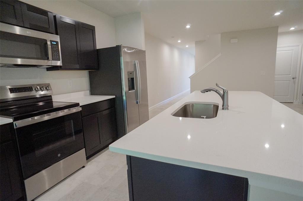A modern kitchen features dark cabinets, stainless steel appliances, and a white quartz island countertop — 12016 GRIZZLY LANE, NEW PORT RICHEY, FL