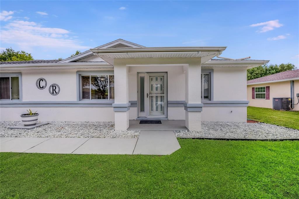 A white single-story house features a covered front porch, gray trim, and a gravel yard — 10452 SW 62ND TERRACE ROAD, OCALA, FL