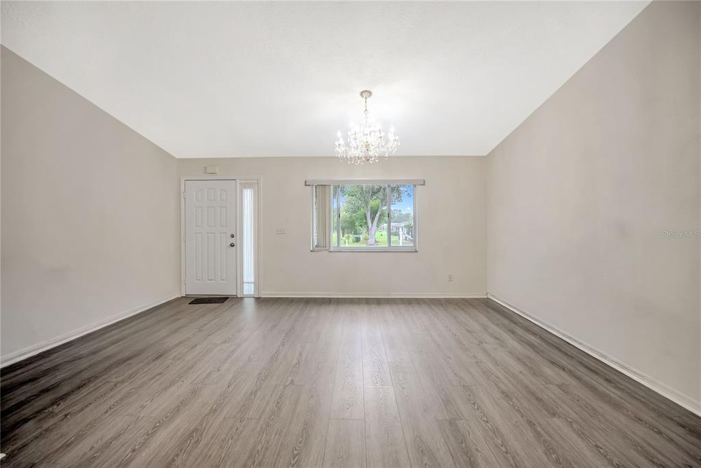 An empty room features light-colored walls, gray wood-look flooring, a chandelier, and a front door — 10452 SW 62ND TERRACE ROAD, OCALA, FL