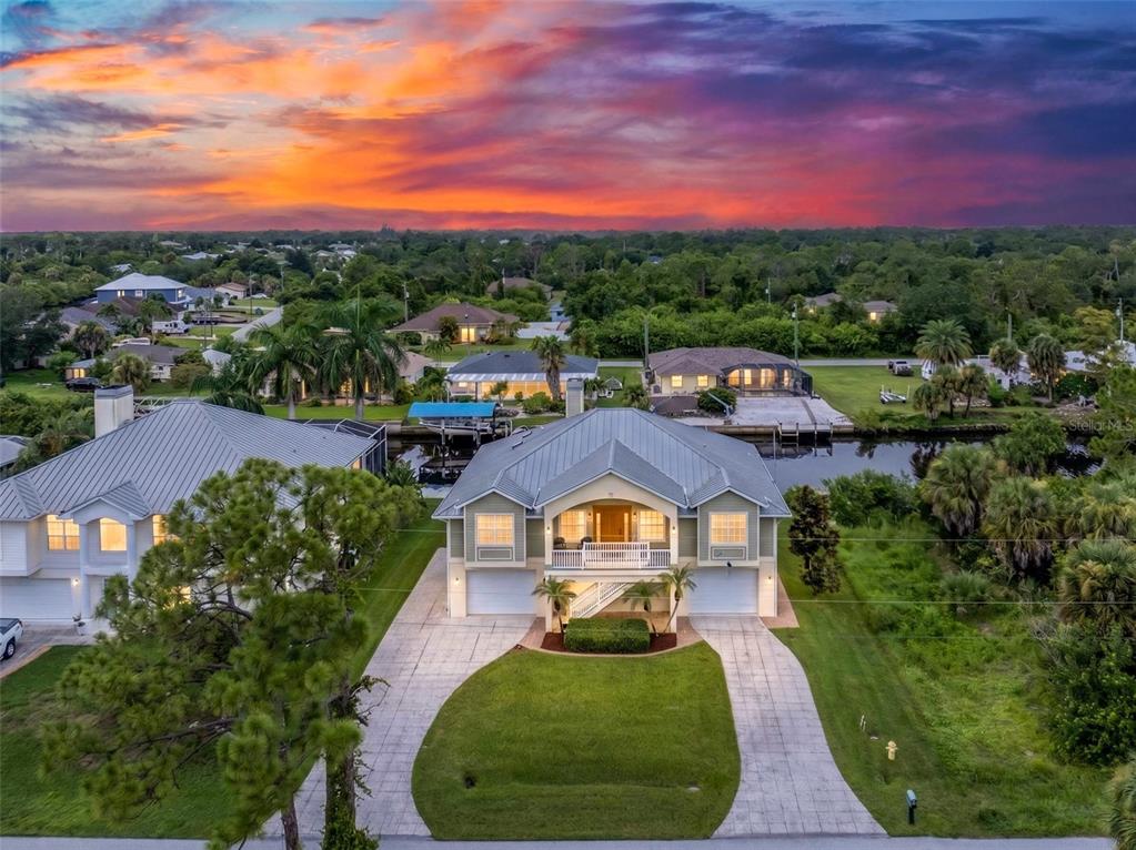 An elevated two-story house with a metal roof and a driveway sits near a canal — 4219 SPIRE STREET, PORT CHARLOTTE, FL