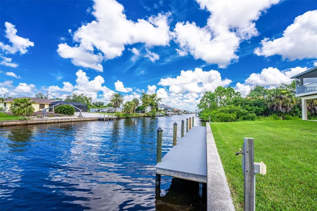 A wooden dock extends into a canal bordered by a grassy lawn and residential homes — 4219 SPIRE STREET, PORT CHARLOTTE, FL