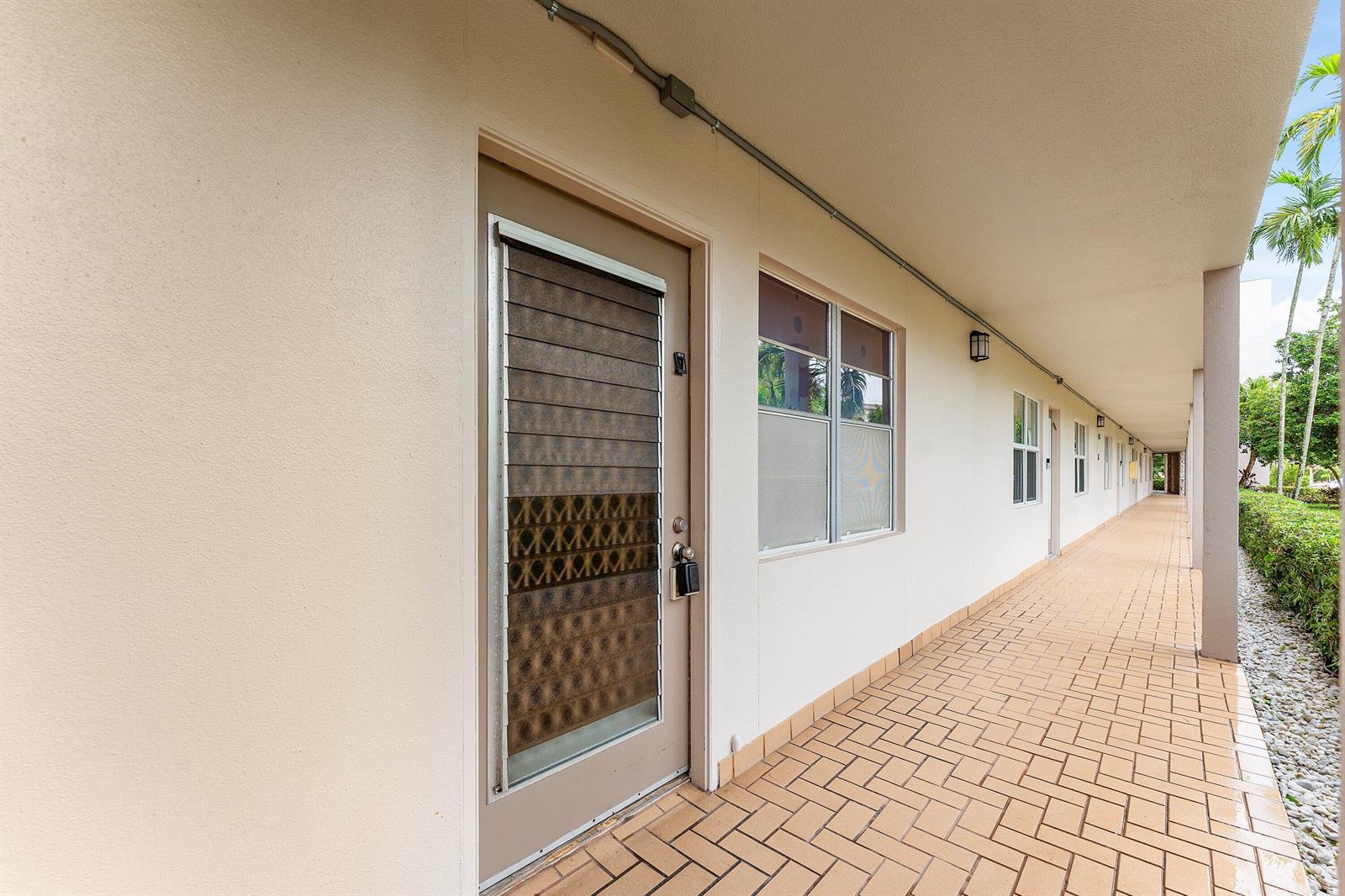 An exterior walkway with tiled flooring leads past several apartment doors and windows — 3301 Aruba Way # C1, Coconut Creek FL 33066, COCONUT CREEK, FL