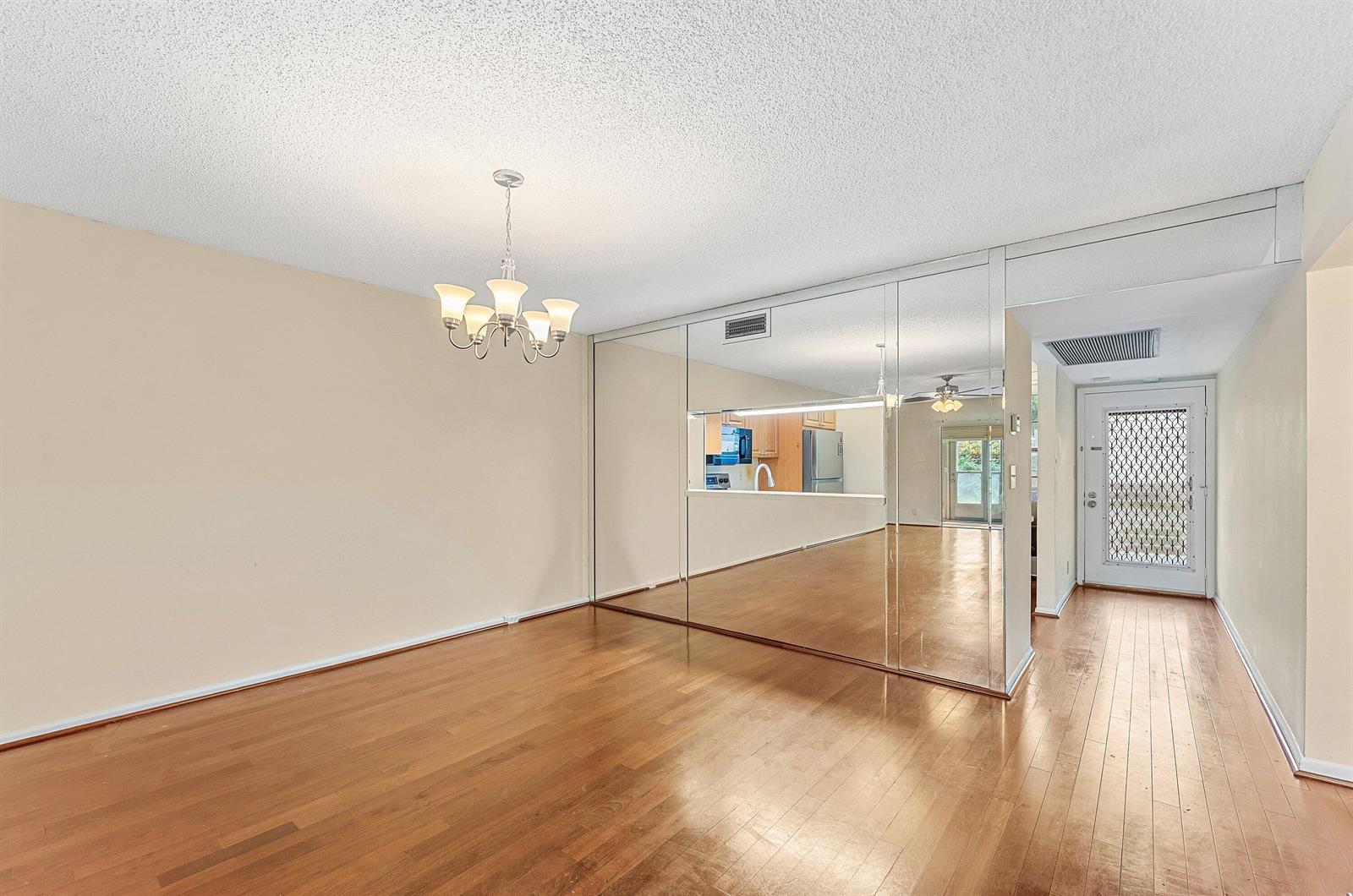 An empty dining room features hardwood floors, a chandelier, and a large mirrored accent wall — 3301 Aruba Way # C1, Coconut Creek FL 33066, COCONUT CREEK, FL
