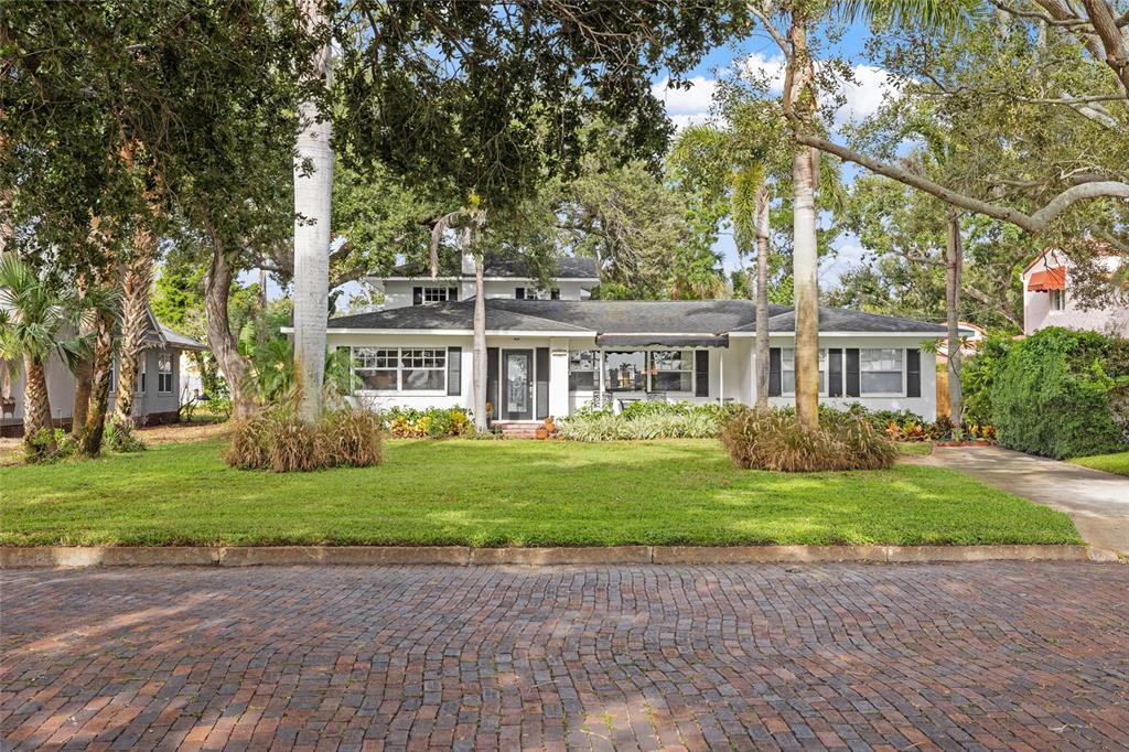 A white single-story house with a dark roof sits behind a brick street and lawn — 311 SUNSET DRIVE N, ST PETERSBURG, FL