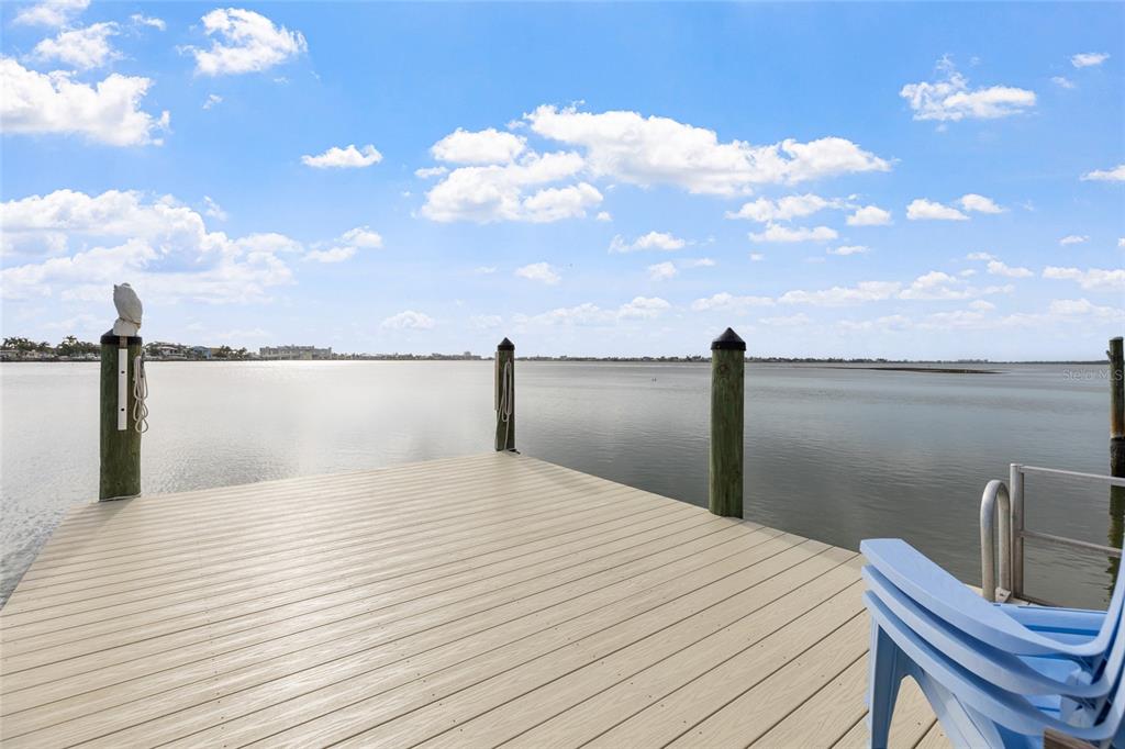 A wooden dock extends over calm water under a blue sky with scattered clouds — 311 SUNSET DRIVE N, ST PETERSBURG, FL