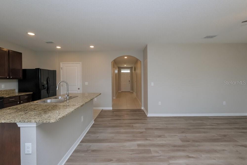 A kitchen with granite countertops and dark cabinets opens to a living area and hallway — 14133 ARBOR PINES DRIVE, RIVERVIEW, FL