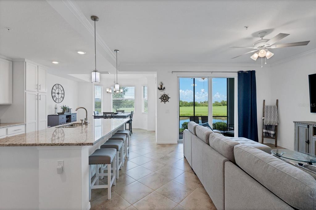 An open-concept kitchen and living area features a granite island, tile flooring, and sliding doors — 14071 HERITAGE LANDING BOULEVARD UNIT 316, PUNTA GORDA, FL