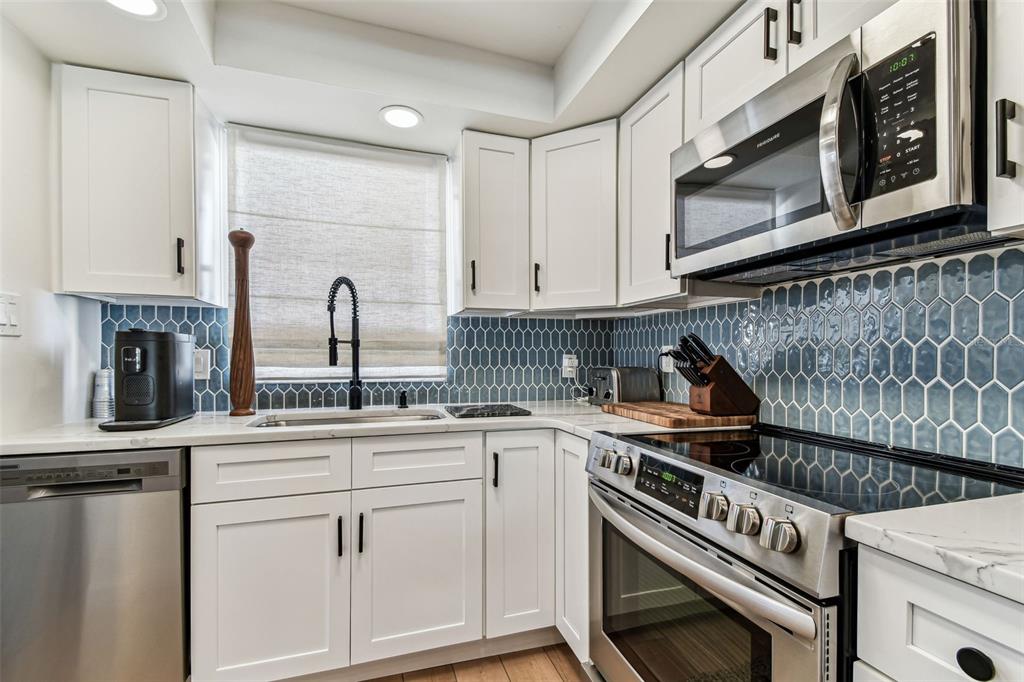 A kitchen features white cabinets, a marble-topped island, stainless steel appliances, and blue tile backsplash — 620 EDGEWATER DRIVE UNIT 204, DUNEDIN, FL