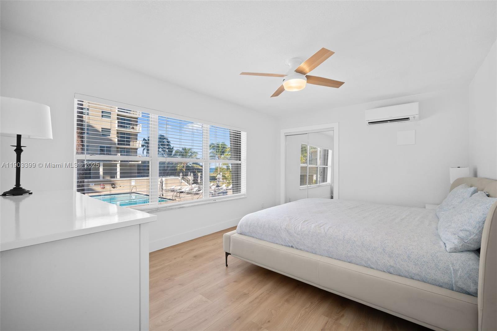 A bedroom features a bed, a ceiling fan, light wood floors, and a pool view — 9241 Collins Ave # 11, Surfside FL 33154, SURFSIDE, FL
