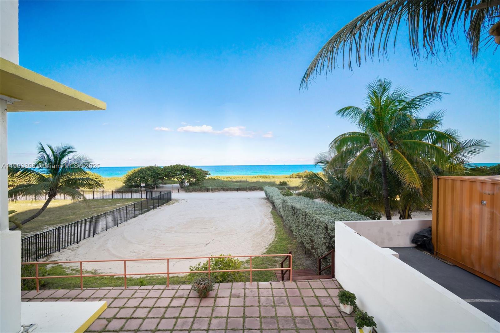 An elevated view shows a sandy area, palm trees, and the ocean beyond a fence — 9241 Collins Ave # 11, Surfside FL 33154, SURFSIDE, FL