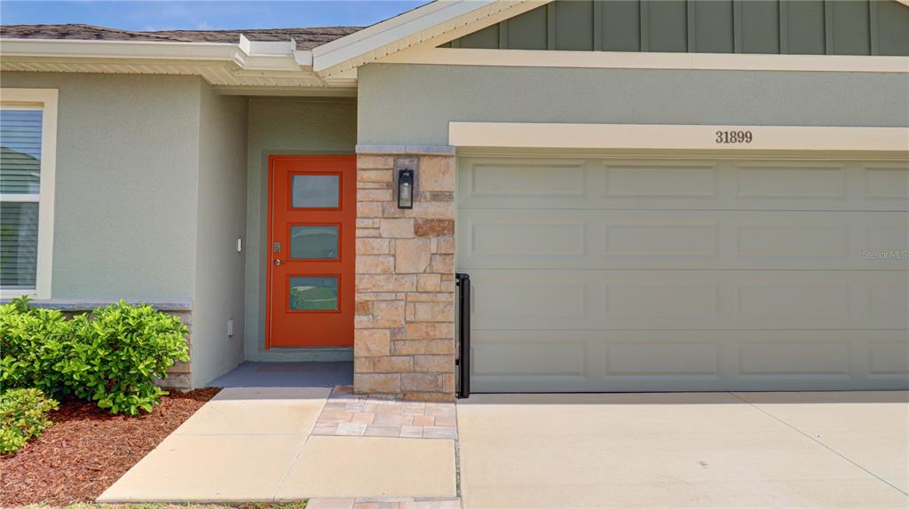The exterior of a house features a bright orange front door and a stone-accented garage — 31899 OYSTER TRELLIS LANE, WESLEY CHAPEL, FL