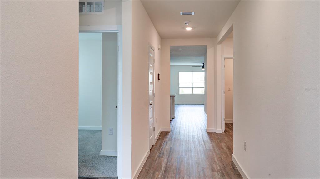 A hallway with wood-look flooring leads to a bright living area with a ceiling fan — 31899 OYSTER TRELLIS LANE, WESLEY CHAPEL, FL