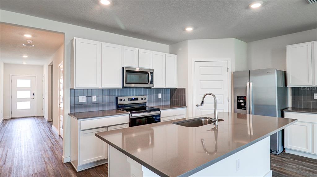 A kitchen features white cabinets, gray countertops, stainless steel appliances, and a central island — 31899 OYSTER TRELLIS LANE, WESLEY CHAPEL, FL