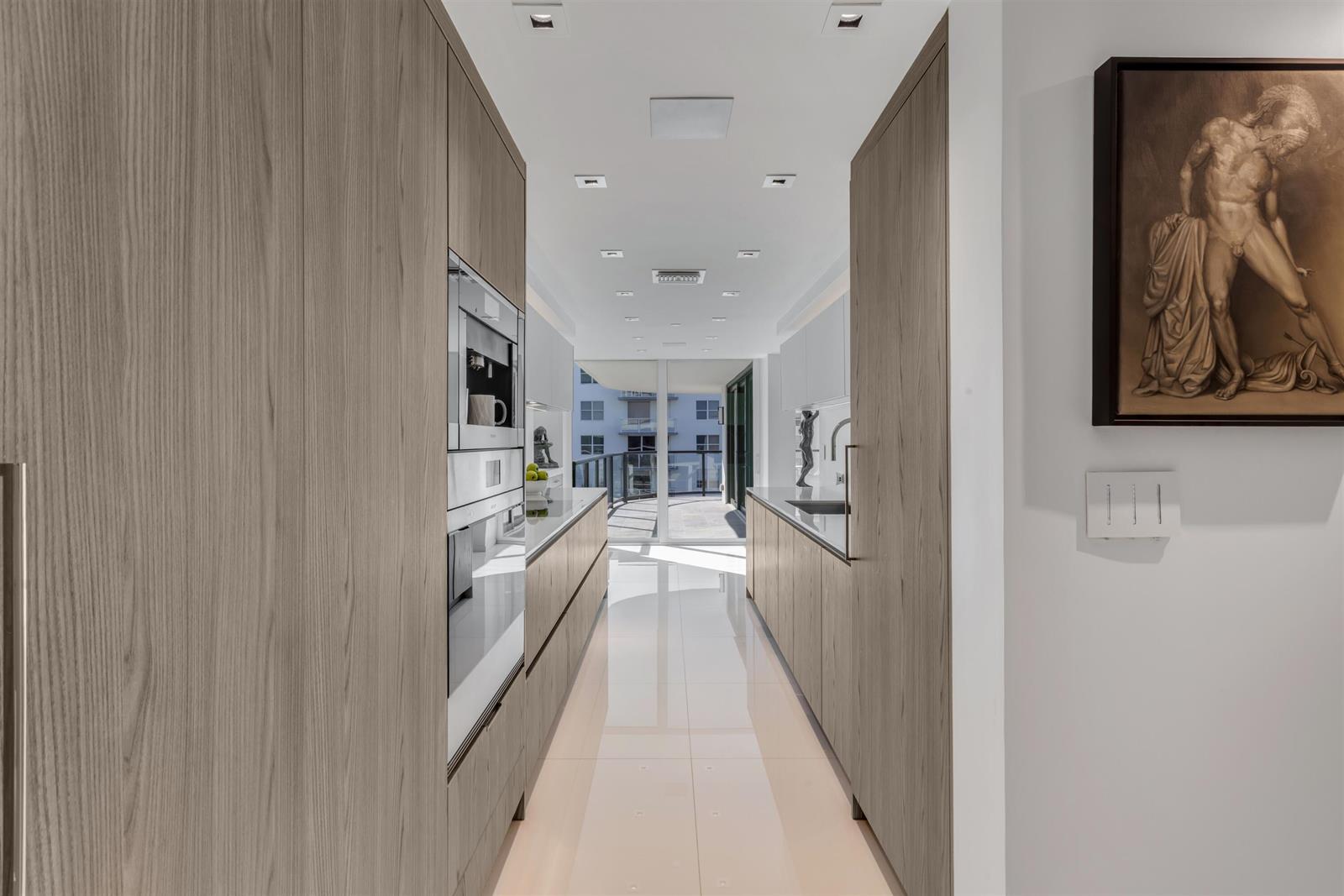 A modern galley kitchen features wood-paneled cabinetry, white countertops, and a view of a balcony — 3440 S Ocean Boulevard # 708s, Palm Beach FL 33480, PALM BEACH, FL