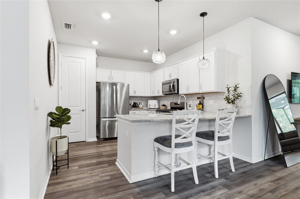 A modern kitchen features white cabinets, stainless steel appliances, a breakfast bar, and wood flooring — 6308 MOORING LINE CIRCLE, APOLLO BEACH, FL
