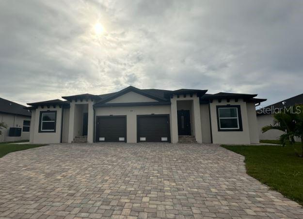 A single-story duplex with two garages and a paved driveway under a cloudy sky — 55 BOUNDARY BOULEVARD UNIT A, ROTONDA WEST, FL