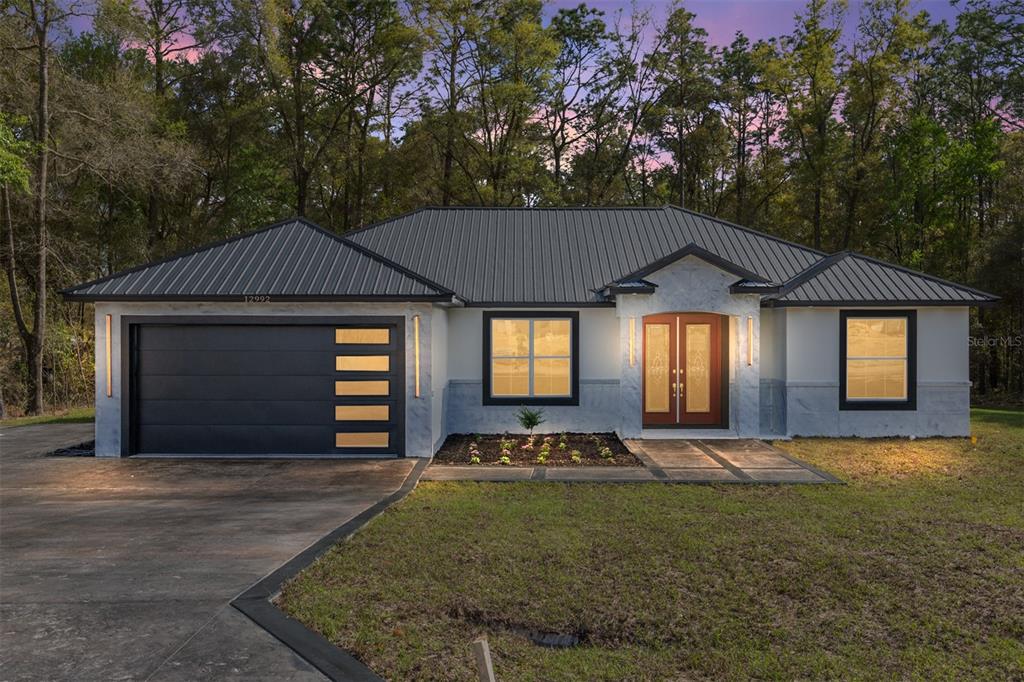 A single-story house with a metal roof, gray stucco exterior, and a dark garage door — 12992 SW 64TH LANE, OCALA, FL