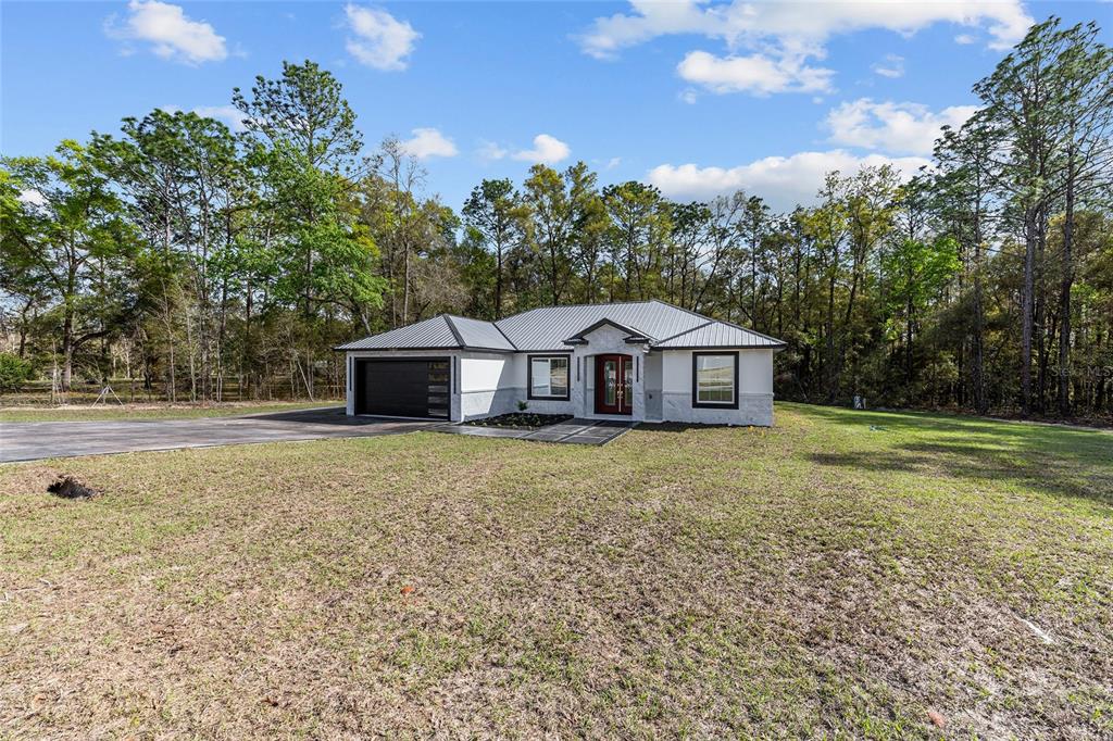 A single-story house with a metal roof, white stucco exterior, and a two-car garage — 12992 SW 64TH LANE, OCALA, FL