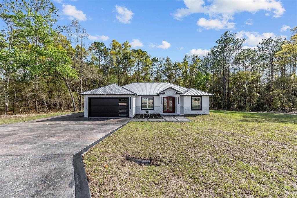 A single-story house with a metal roof, black garage door, and red front door — 12992 SW 64TH LANE, OCALA, FL