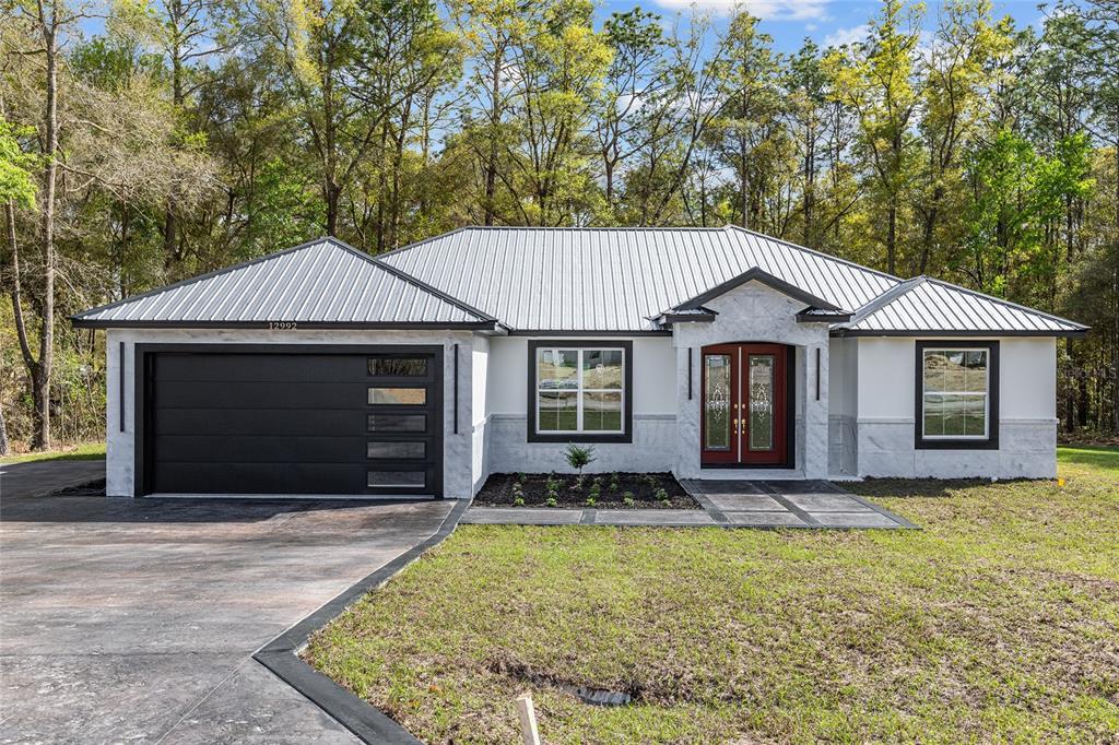 A single-story house with a metal roof, white stucco walls, and a black garage door — 12992 SW 64TH LANE, OCALA, FL