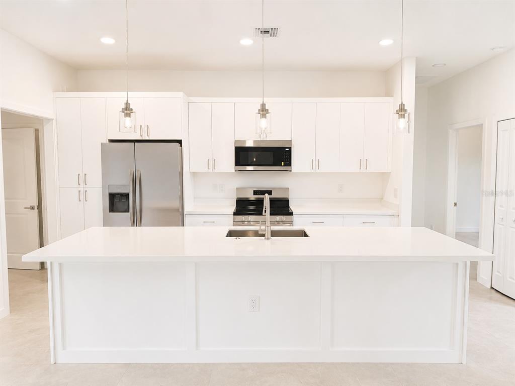 A modern kitchen features white cabinetry, stainless steel appliances, and a large central island — 2907 W 25 ST W. STRATA VII STREET, LEHIGH ACRES, FL