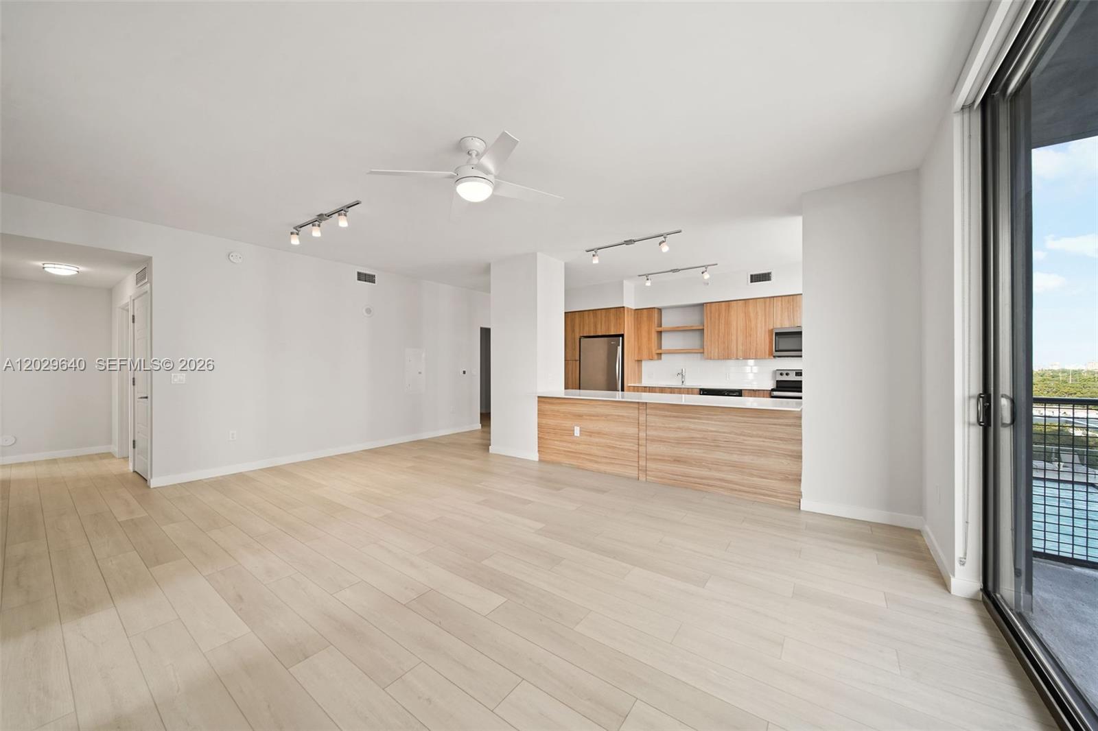 An open-concept living area features light wood flooring, a kitchen with wood cabinetry, and a balcony — FORT LAUDERDALE, FL