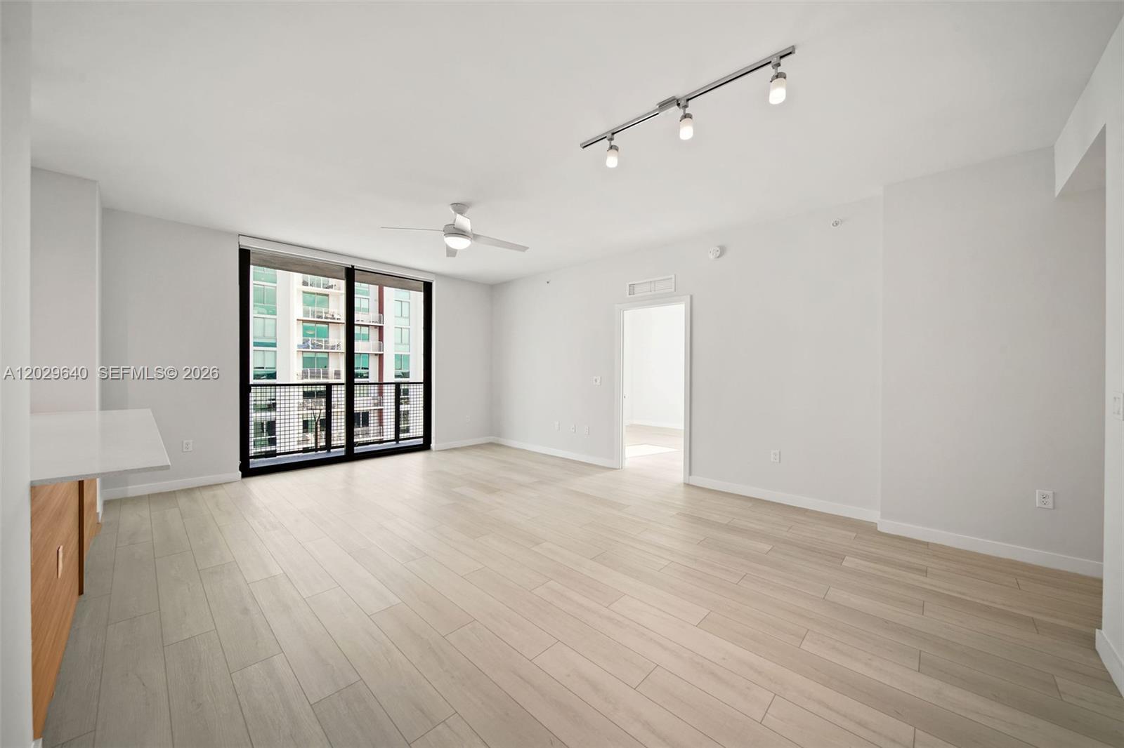 A bright, empty living room features light wood-look flooring, a ceiling fan, and a balcony — FORT LAUDERDALE, FL