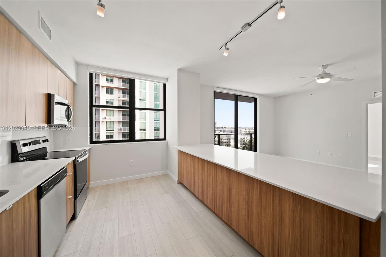 A modern kitchen features wood-toned cabinetry, white countertops, stainless steel appliances, and light flooring — FORT LAUDERDALE, FL