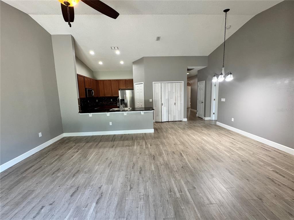 An open-concept living area features light wood-look flooring, gray walls, and an adjacent kitchen — 764 CHACALL LOOP, MOUNT DORA, FL
