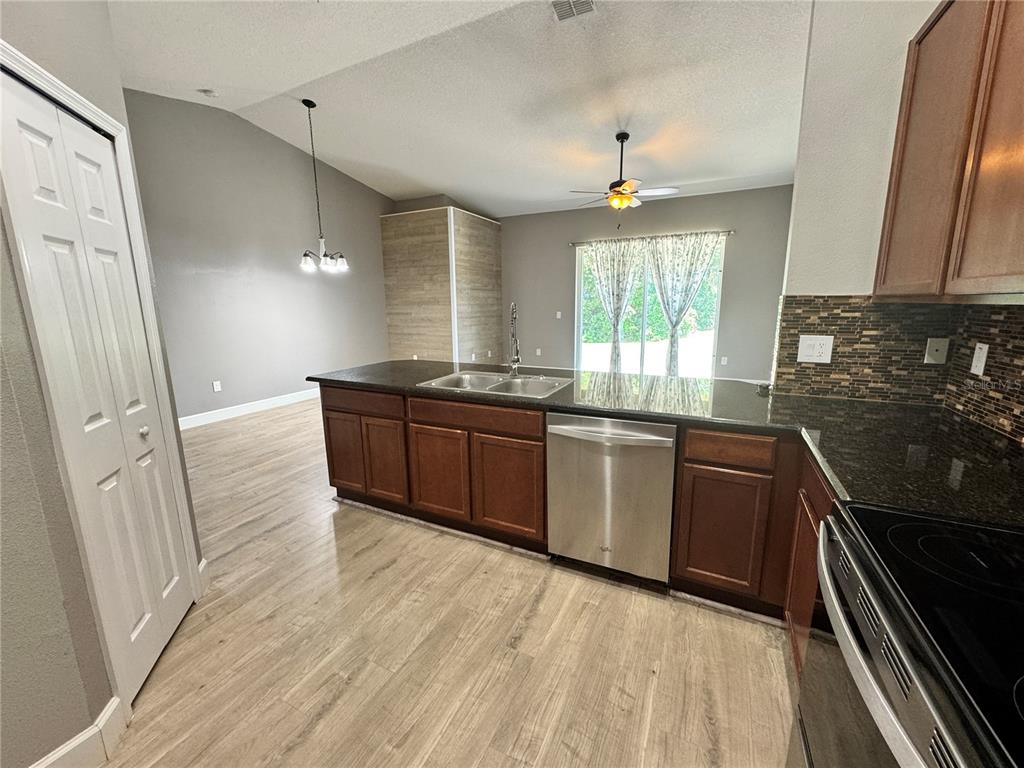 A kitchen with dark wood cabinets, granite countertops, stainless steel appliances, and light wood flooring — 764 CHACALL LOOP, MOUNT DORA, FL