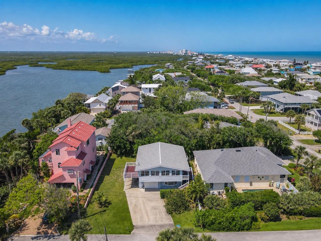 An aerial view shows several houses near a body of water and a distant coastline — 824 GARFISH AVENUE, NEW SMYRNA BEACH, FL