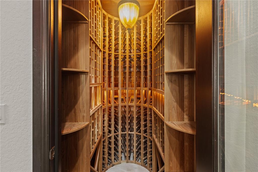A small, curved wooden wine cellar features custom bottle racking and a central pendant light — 1008 PASEO DEL RIO NE, ST PETERSBURG, FL