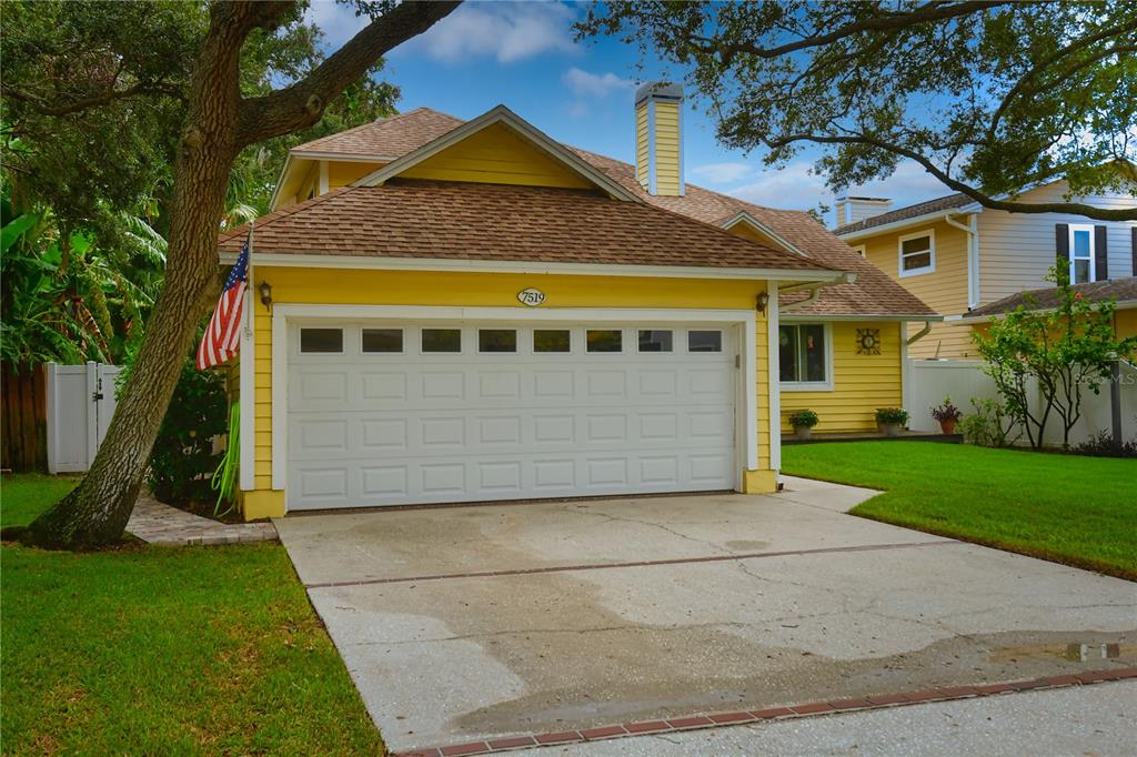 A yellow house with a two-car garage and a concrete driveway under a tree — 7519 HARBOR VIEW WAY, SEMINOLE, FL