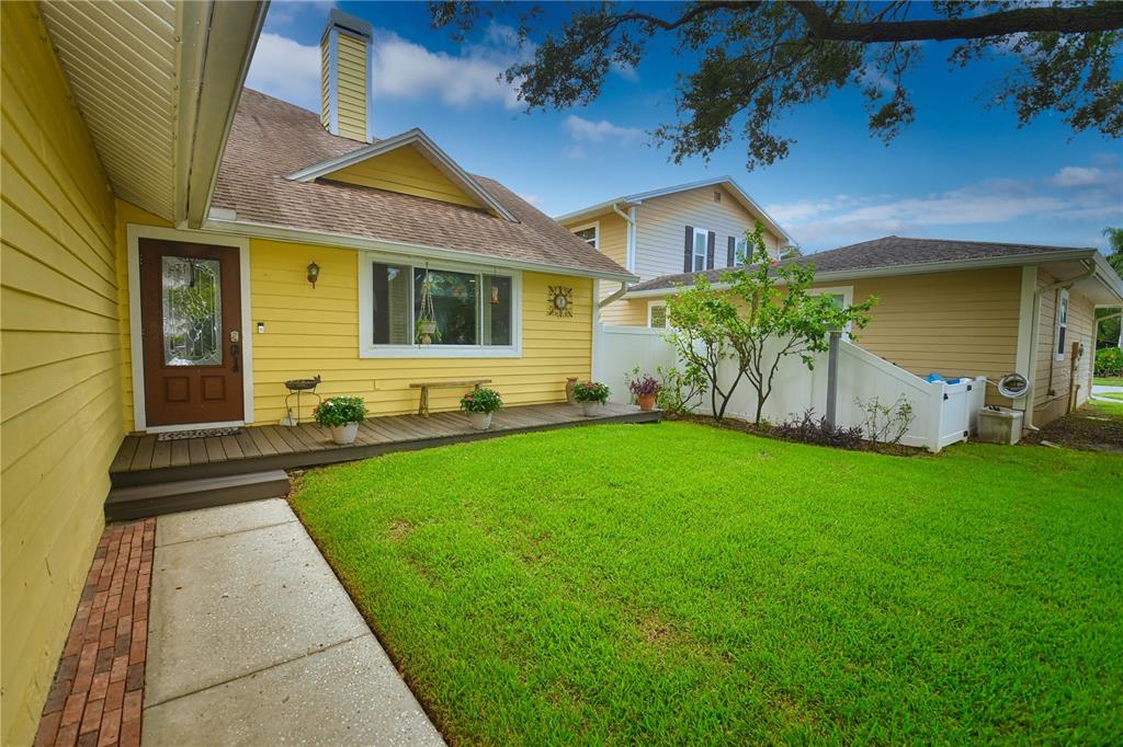 A yellow house with a wooden deck, brick walkway, and green lawn under a blue sky — 7519 HARBOR VIEW WAY, SEMINOLE, FL